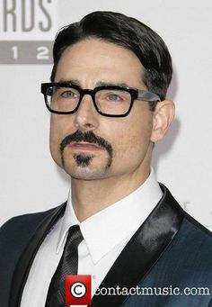 a man wearing glasses and a suit with a mustache on the red carpet at an awards event