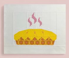 a piece of fabric with a yellow cake on it and pink ribbon in the middle