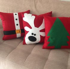 three christmas pillows on a couch with santa's reindeer head and tree in the center