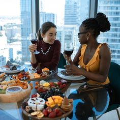 two women sitting at a table with plates of food and wine in front of them