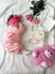 a baby laying on top of a bed next to a pink teddy bear