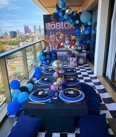 a table set up for a birthday party with blue and white balloons on the wall