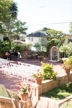 an outdoor ceremony setup with white chairs and flowers in planters on the side walk