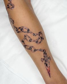 a person's arm with chains and a dagger tattoo on the left side of their leg