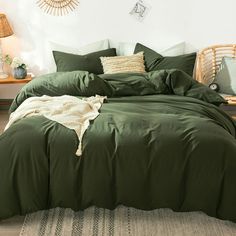 a bed with green comforter and pillows in a white room next to a wicker chair