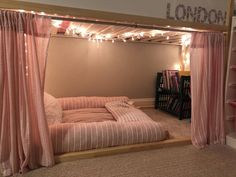 there is a bed with pink curtains and lights on the headboard, along with bookshelves