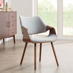 a grey chair with wooden legs sits in front of a dresser and side table on the floor