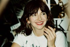 a woman smiling and holding her hand to her face while wearing a white t - shirt