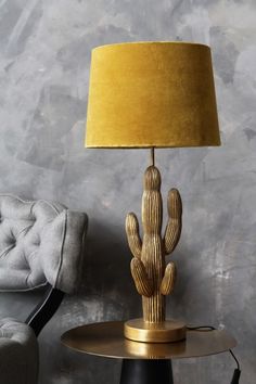 a gold cactus lamp sitting on top of a table next to a gray chair with a blue shade