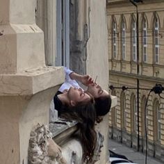 a woman leaning on the side of a building with her head hanging over a ledge