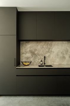 a modern kitchen with black cabinets and marble counter tops, along with a yellow bowl on the sink