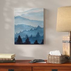 a painting is hanging on the wall above a desk with a lamp and other items