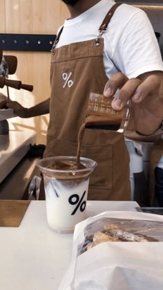 a man pouring something into a cup on top of a counter next to a bag