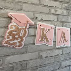 pink and gold graduation banner hanging on brick wall