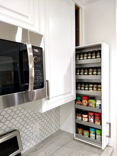 a kitchen with white cabinets and stainless steel microwave above the stove is filled with spices