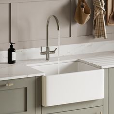 a white kitchen sink sitting under a faucet next to a wall mounted soap dispenser