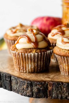 three cupcakes with caramel and white frosting sitting on a wooden board