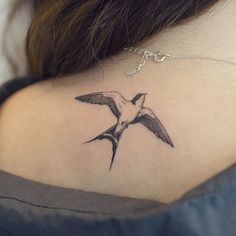 a small tattoo on the back of a woman's neck, with a bird flying above it