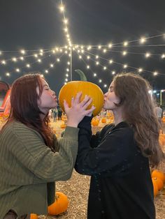 two women are touching each other with pumpkins on display in the background at night