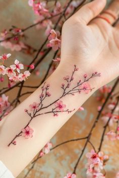 a woman's arm with pink flowers and branches tattooed on the left side of her wrist