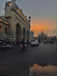 the sun is setting over a busy street with cars, motorcycles and people on it