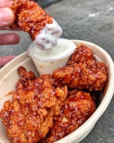 a person dipping something into a bowl with chicken wings on it and sauce in the middle