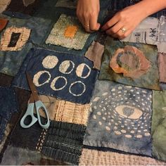 a woman is cutting fabric with scissors on a quilted tablecloth that has various patterns and shapes