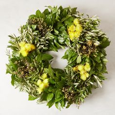 a green wreath with yellow flowers and greenery on the front is displayed against a white background