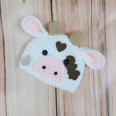 a crocheted cow hat with brown ears on top of a wooden floor next to a pair of scissors