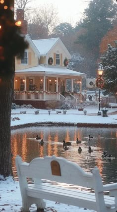 a white bench sitting in front of a lake covered in snow next to a house