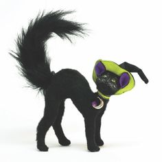 a black cat with purple eyes and tail standing next to a white background wearing a green hat