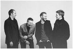 three men standing next to each other in front of a white wall and one is laughing