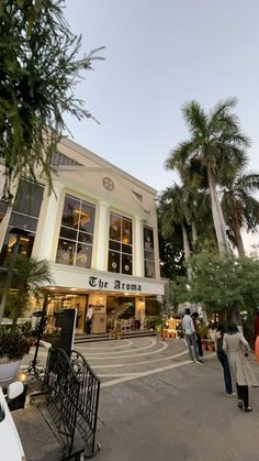 people walking in front of a building with many windows and palm trees on the street