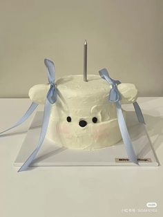 a white cake with blue ribbon around the edges and a bear face on it's side