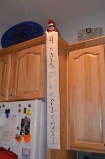 the elf is sitting on top of the kitchen cabinets with his name written on it