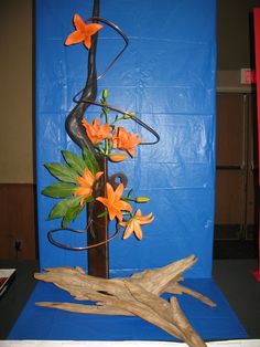 a vase with orange flowers in it sitting on a blue table cloth covered surface next to a tree branch