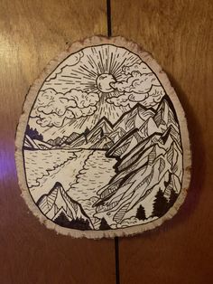 a piece of wood with a drawing on it that has mountains and trees in the background