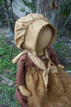 a cloth doll with a bonnet and dress sitting on the ground next to a tree