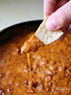 a hand holding a tortilla chip and dipping it into a bowl of chili