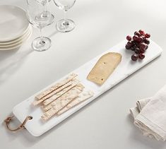 cheese, crackers and grapes are arranged on a white platter next to wine glasses