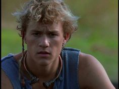 a young man with blonde hair wearing a blue shirt and silver necklace on his neck