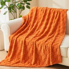 an orange blanket is draped on a white couch in front of a potted plant