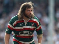 a man with long hair wearing a green and red striped rugby shirt standing in front of a crowd