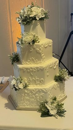 a three tiered wedding cake with white flowers and greenery