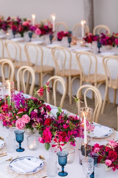 the table is set with white linens and blue vases filled with pink flowers