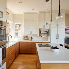 a kitchen with wooden floors and white cabinets, an island countertop and stainless steel appliances