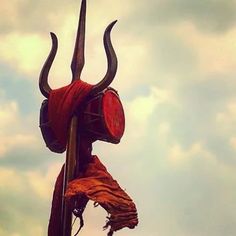 a red sculpture with long horns on it's head is shown in front of a cloudy sky