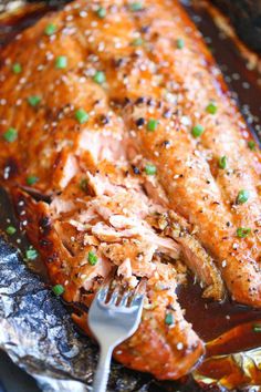 a piece of salmon with sauce and green onions on it is being eaten by a fork