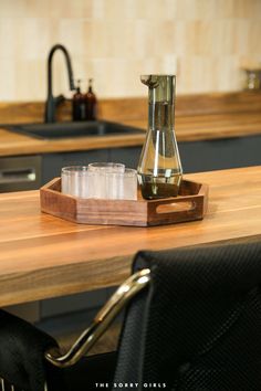 a wooden tray with glasses on top of a kitchen counter next to an oven and sink