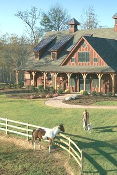 two horses are standing in front of a large house with a wooden fence around it